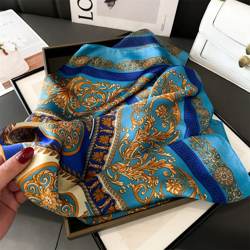 Foulard di Seta "Bandana Miami" 70x70 in blu e oro, esposto in scatola aperta su tavolo elegante.
